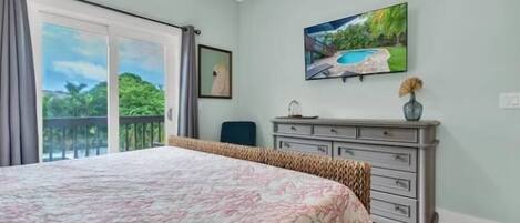A bedroom with a large bed, a dresser, a painting, and a balcony with a view.