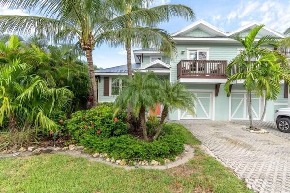 A two-story house with a front porch, a garage, and a landscaped garden with palm trees and shrubs. - 3BR Beach Home heated Pool, Decks & BBQ (Holmes Beach)