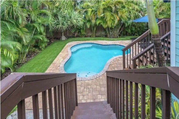 Un jardin avec une piscine, entouré d’une végétation luxuriante et doté d’une terrasse en bois.
