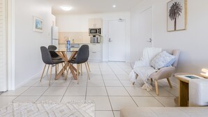 A modern living room with a dining area, a kitchen in the background, and a door leading to another room. - Narli Shores • Coastal Studio for 4 • Private Spa (Agnes Water)