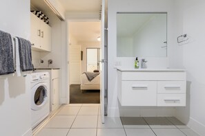 A modern bathroom with a built-in washing machine, a large mirror, and a walk-in shower. - Narli Shores • Coastal Studio for 4 • Private Spa (Agnes Water)