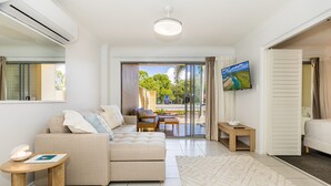 A modern living room with a sofa, a TV, and a view of the outdoors. - Narli Shores • Coastal Studio for 4 • Private Spa (Agnes Water)