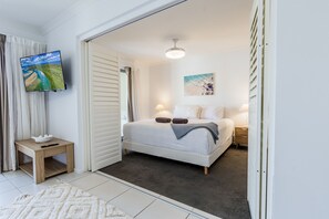 A bedroom with a bed, bedside tables, a TV, and a painting. - Narli Shores • Coastal Studio for 4 • Private Spa (Agnes Water)