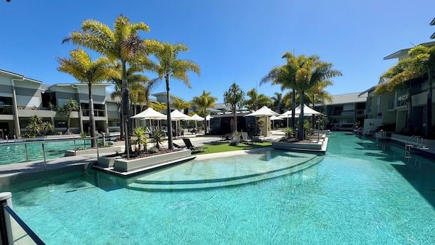 A pool area with clear water, lounge chairs, umbrellas, and palm trees. - Narli Shores • Coastal Studio for 4 • Private Spa (Agnes Water)