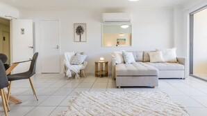 A modern living room with a sofa, chairs, a dining table, and a large mirror. - Narli Shores • Coastal Studio for 4 • Private Spa (Agnes Water)