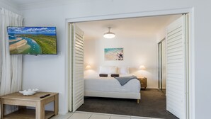 A bedroom with a bed, bedside lamps, a TV, and a painting. - Narli Shores • Coastal Studio for 4 • Private Spa (Agnes Water)