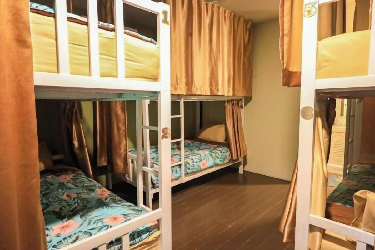 A room with bunk beds, wooden flooring, and curtains.