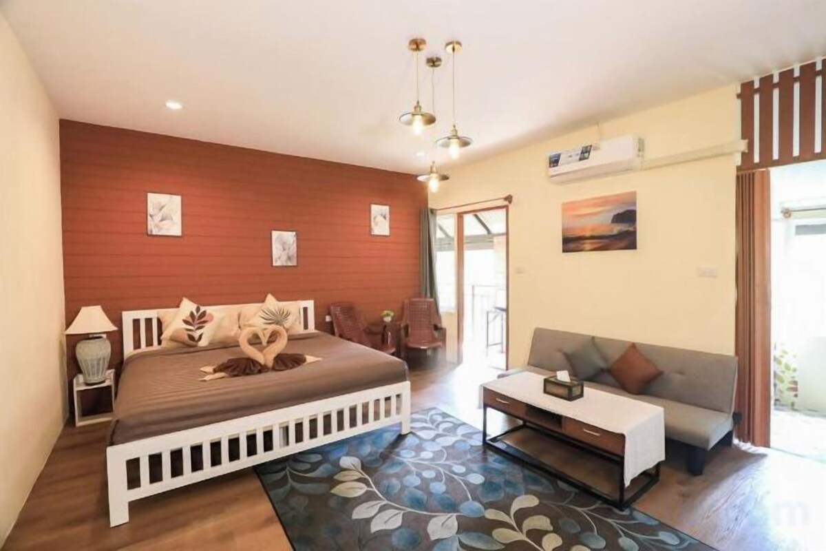 A bedroom with a bed, bedside table, lamp, and a view of the outside.
