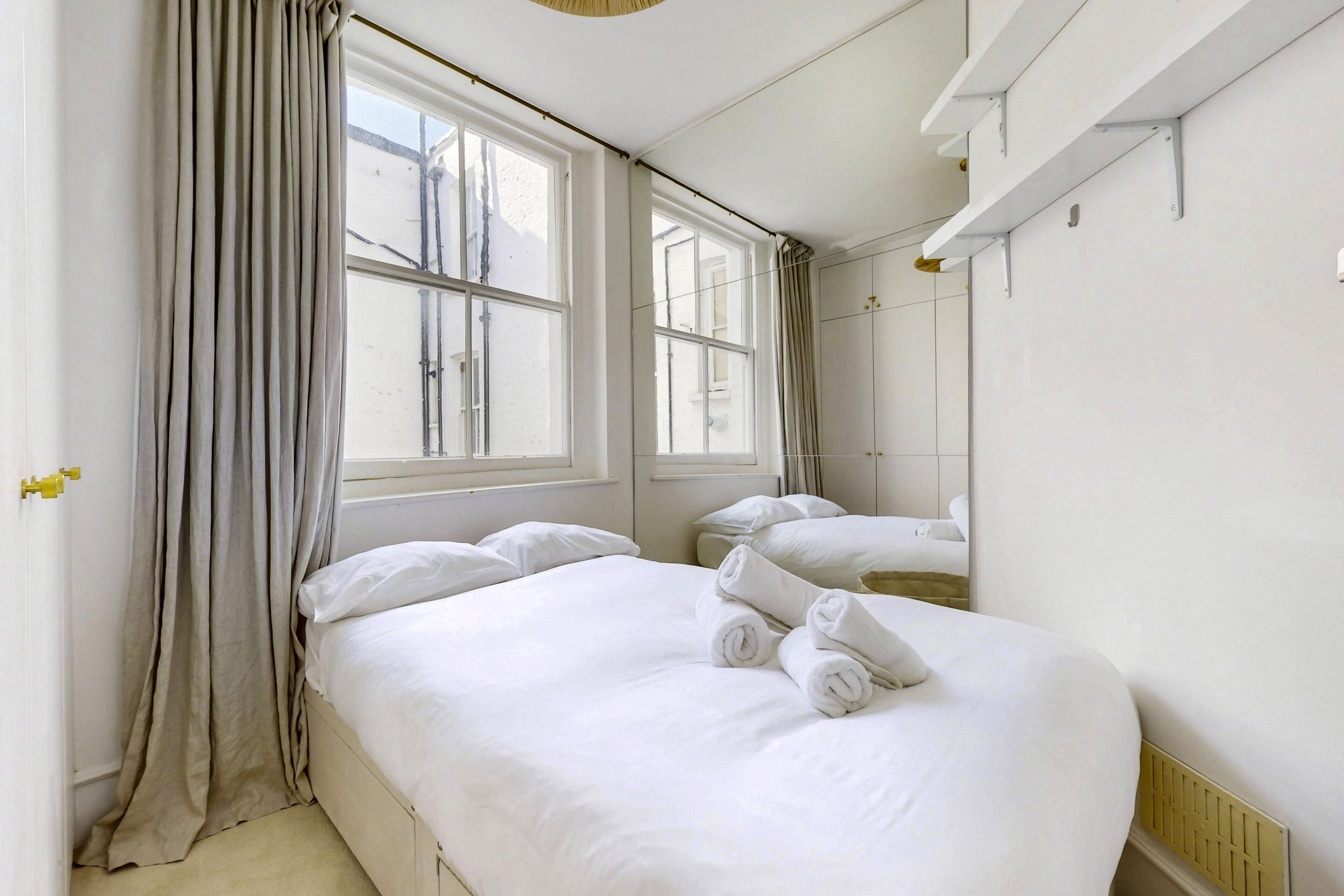 Une chambre d’hôtel avec un grand lit, une fenêtre avec des rideaux, un miroir et une petite table de chevet.