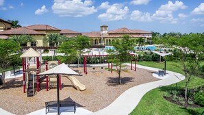 A playground with slides and climbing structures, a pool area, and a building with a red-tiled roof.