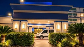 A modern hotel entrance with a white van parked in front, surrounded by well-maintained greenery. - Verta Hotel McAllen (McAllen)