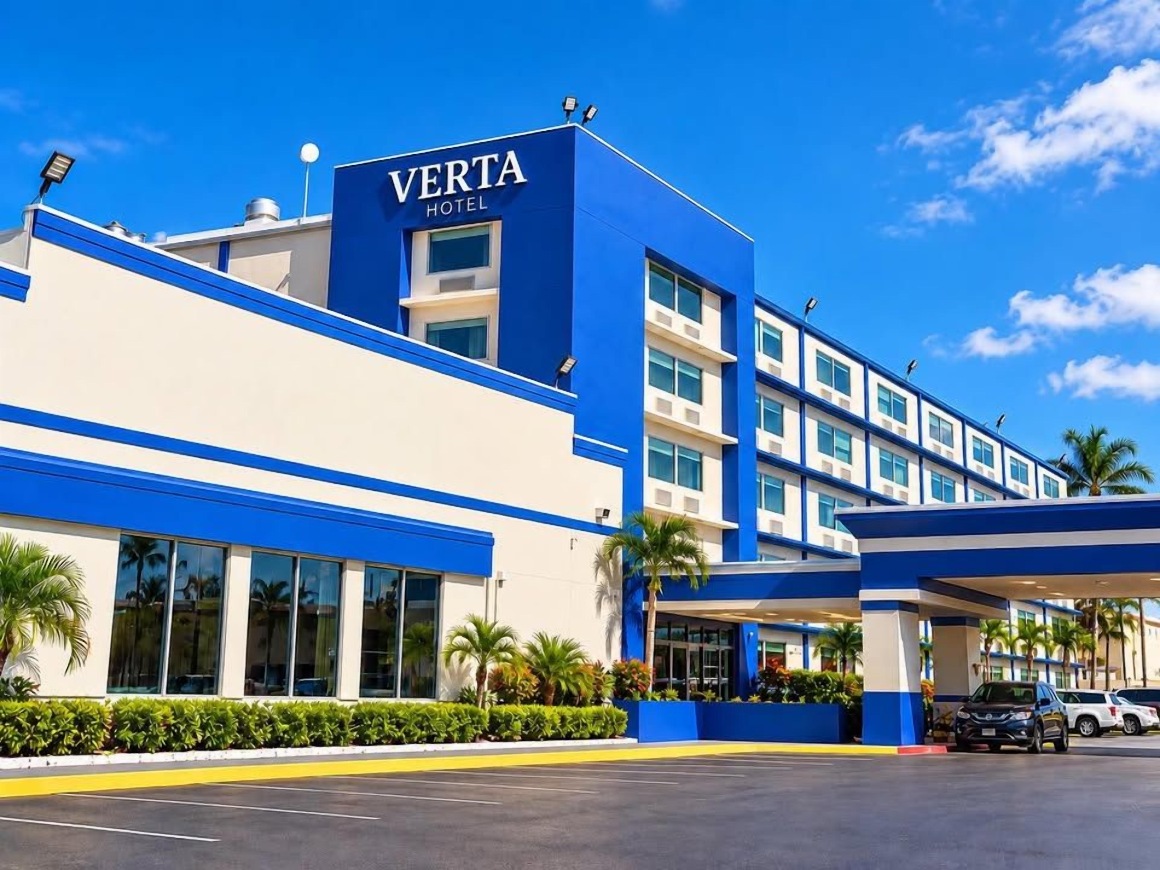 A modern hotel with a blue and white facade, large windows, and a parking lot.