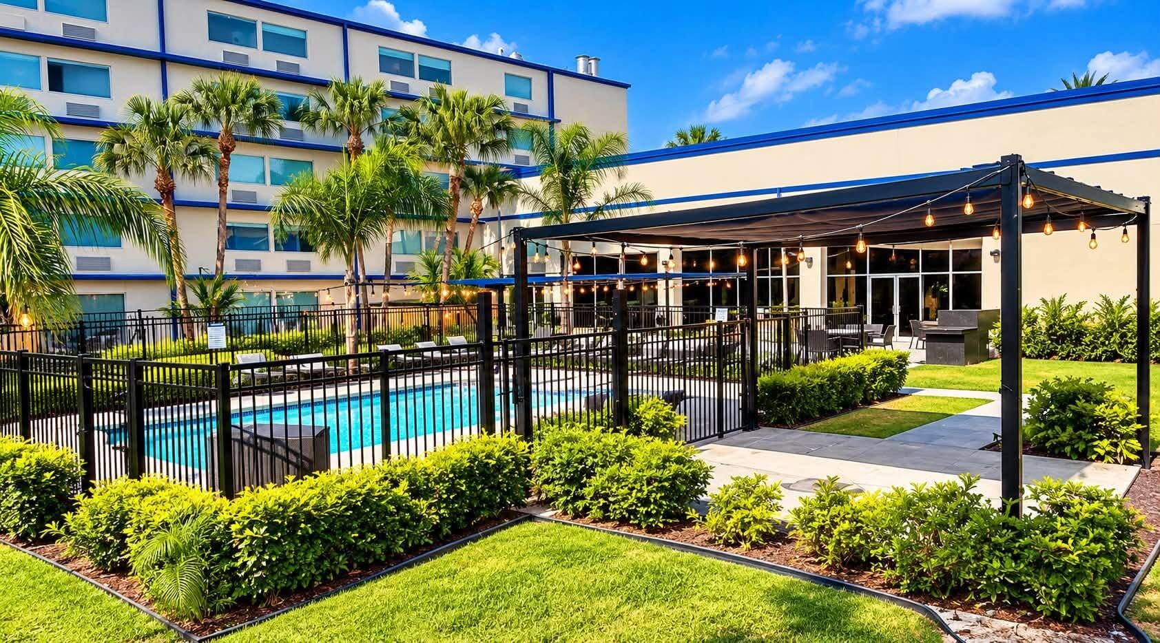 A hotel courtyard with a swimming pool, covered seating area, and lush landscaping.