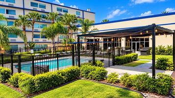 A hotel courtyard with a swimming pool, covered seating area, and lush landscaping.