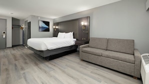 Quarto de hotel moderno com uma cama grande, um sofá cinzento e uma obra de arte pendurada na parede.