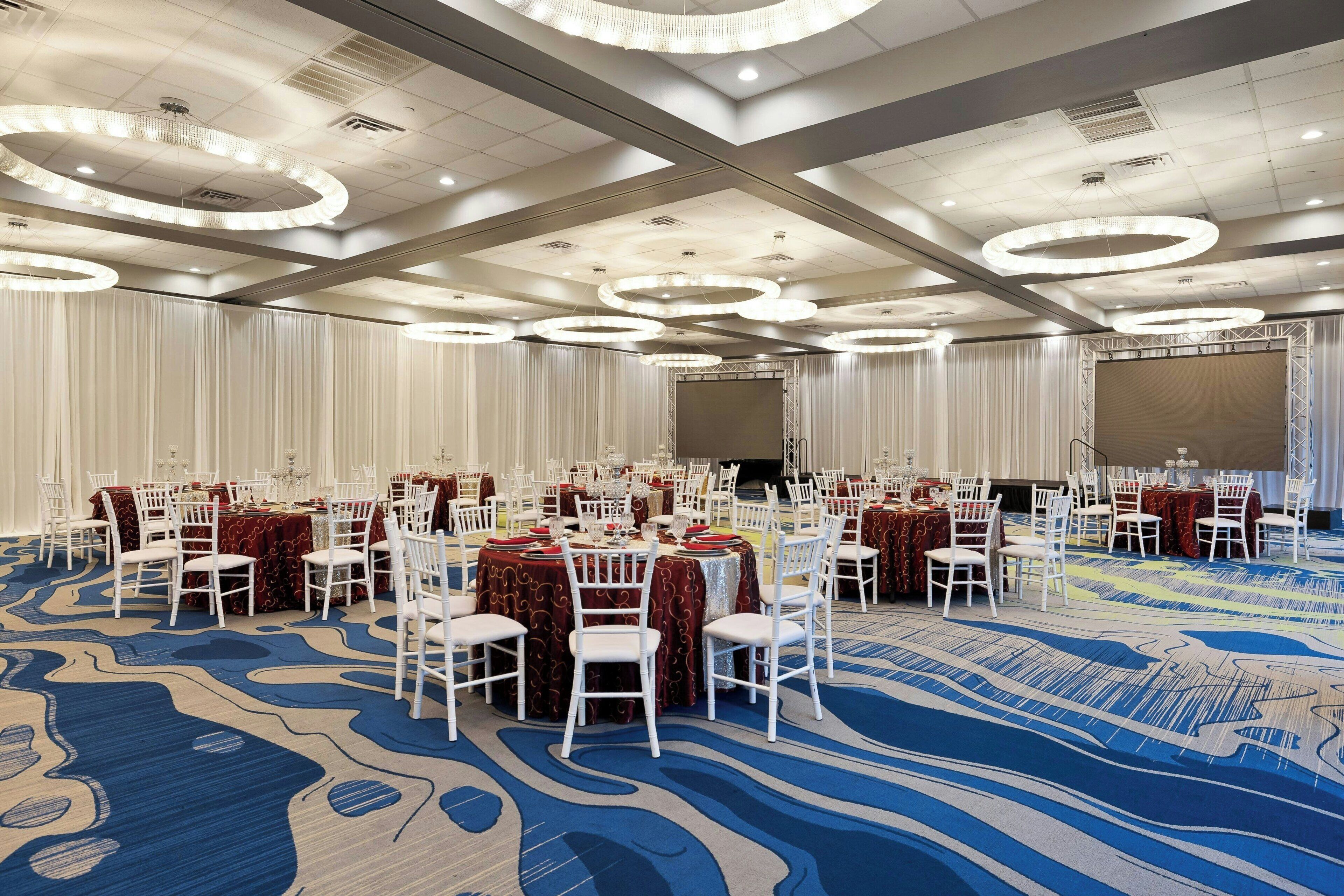 A banquet hall with round tables, white chairs, and a blue carpet.