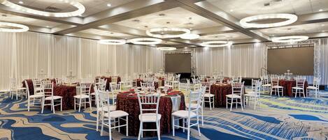 A banquet hall with round tables, white chairs, and a blue carpet.
