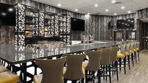 Uma área de bar com um balcão comprido, diversas opções de assento e uma grande televisão de tela plana na parede.