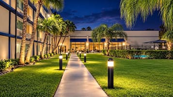 A hotel courtyard with a paved walkway, palm trees, and a pool.