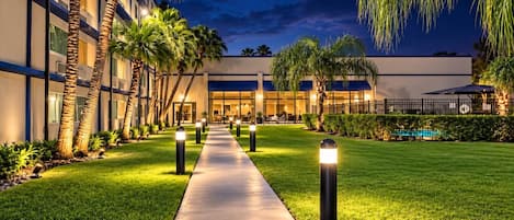 A hotel courtyard with a paved walkway, palm trees, and a pool.