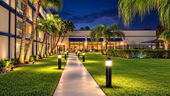 A hotel courtyard with a paved walkway, palm trees, and a pool.