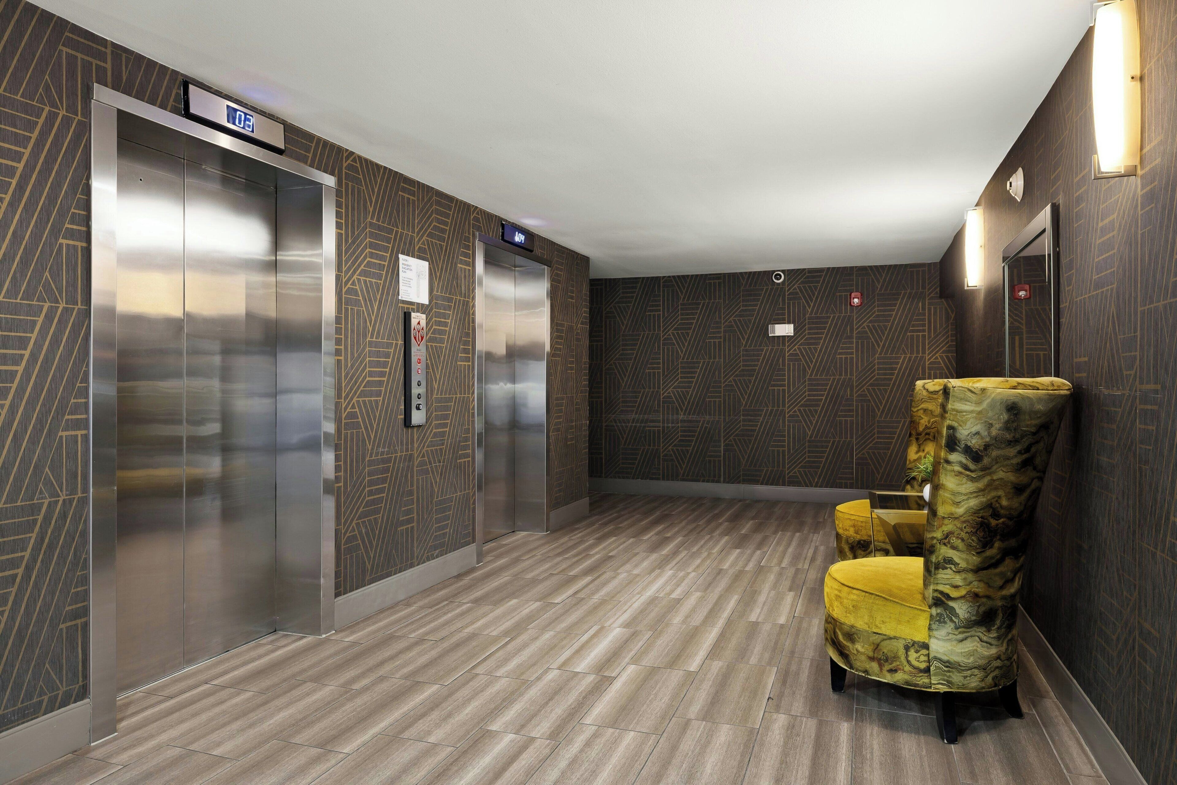 An elevator with a digital display, a chair, and patterned walls.