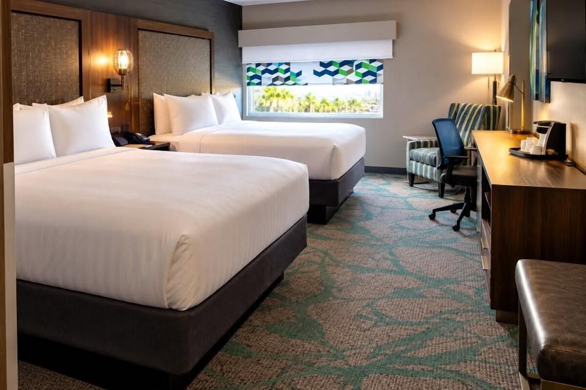 A hotel room with two beds, a desk, a chair, and a TV.