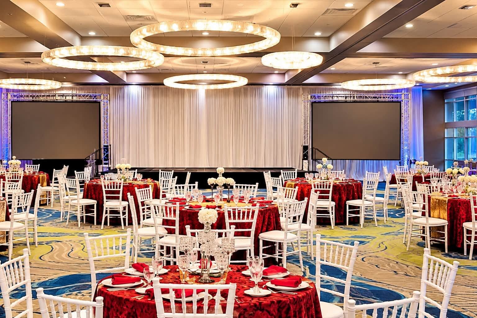Une salle de banquet avec des tables rondes, des chaises blanches et des nappes rouges.