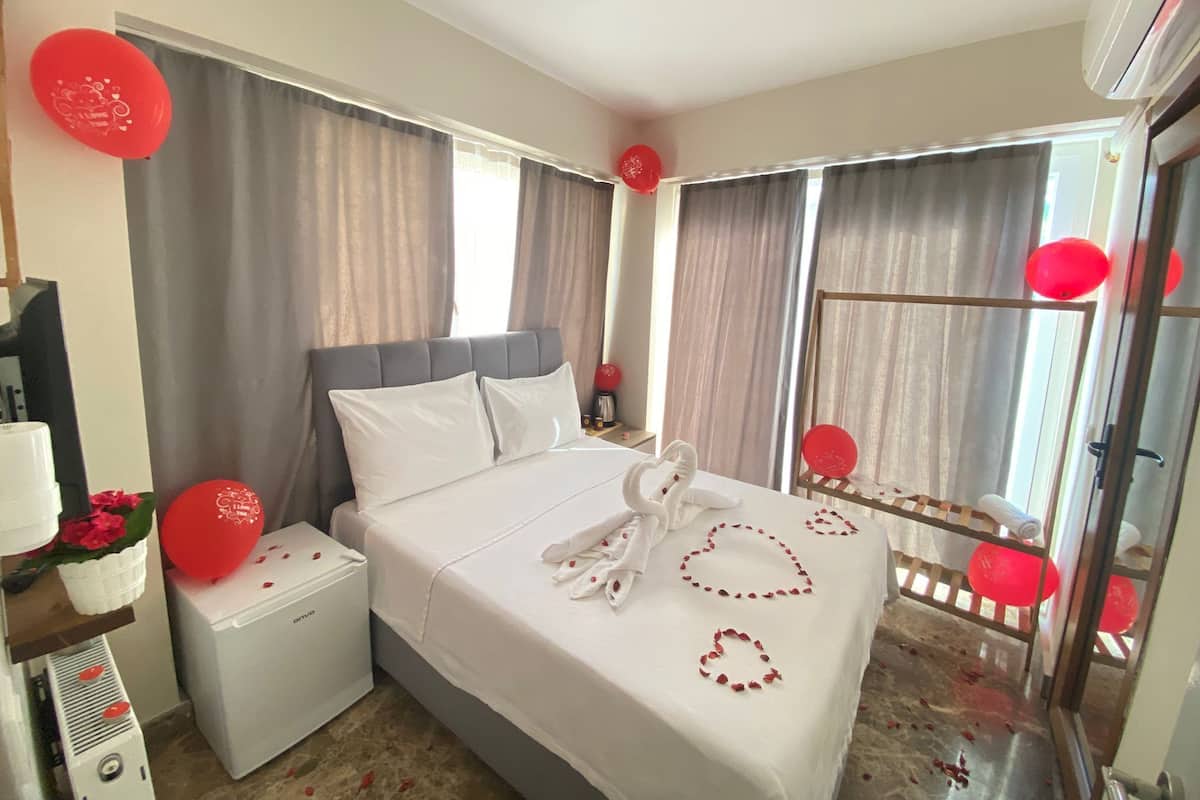 Une chambre d’hôtel avec un lit, des rideaux, une fenêtre, un radiateur et des ballons rouges.