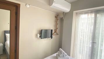 Une chambre d’hôtel comprenant un lit, un téléviseur fixé au mur, un appareil de climatisation, une porte de salle de bain et une fenêtre avec des rideaux.