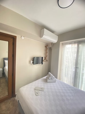 A hotel room with a bed, a wall-mounted TV, an air conditioning unit, a bathroom door, and a window with curtains. - Buyukada Carsi Pansiyon (Adalar)
