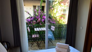 Une chambre d’hôtel avec un lit, une fenêtre donnant sur un balcon et une table avec des chaises à l’extérieur.