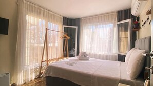 Une chambre d’hôtel avec un grand lit, une échelle en bois, un miroir, un radiateur et une fenêtre avec des rideaux légers.