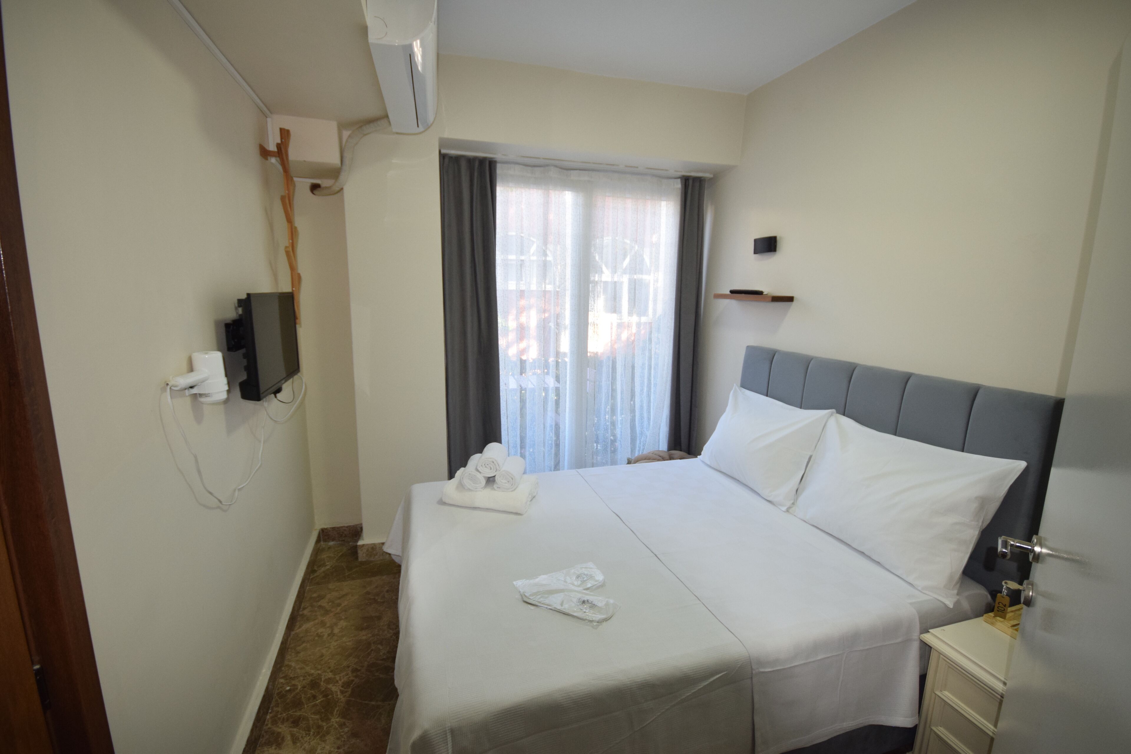A hotel room with a bed, a bedside table, a TV, and a window with curtains.