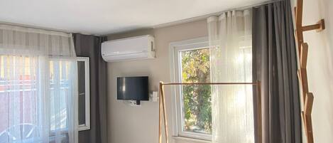Habitación de hotel con cama, televisor montado en la pared, ventana con cortinas y un columpio de madera.