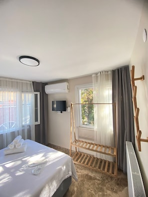 Une chambre d’hôtel avec un lit, un téléviseur fixé au mur, une fenêtre avec des rideaux et une balançoire en bois.