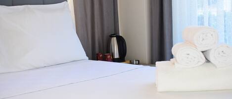 A hotel room with a neatly made bed, a coffee maker, and rolled towels on the side.