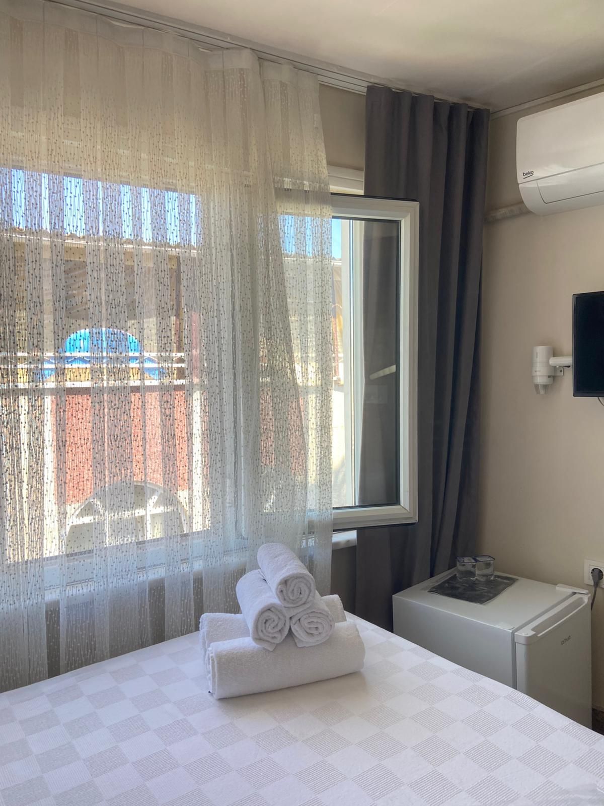 Une chambre d’hôtel avec un lit, une fenêtre avec des rideaux, une petite table avec des verres et un appareil de climatisation.