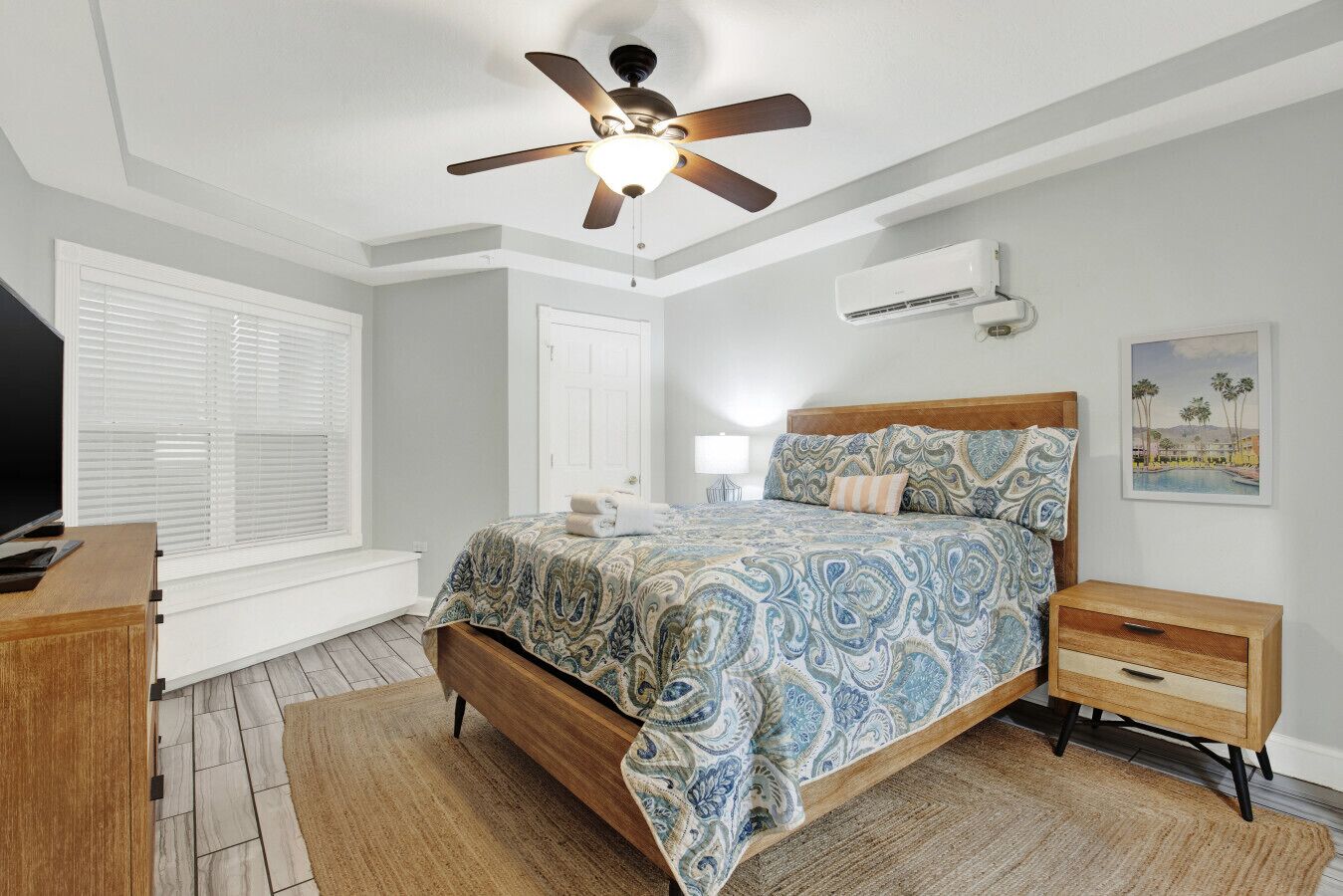Un dormitorio con cama, mesitas de noche, ventilador de techo, equipo de aire acondicionado y una ventana con persianas.