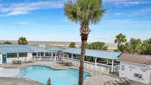 A pool area with lounge chairs and umbrellas, a palm tree, and a view of the beach. - Beachside Colony Resort Unit 222A (Tybee Island)