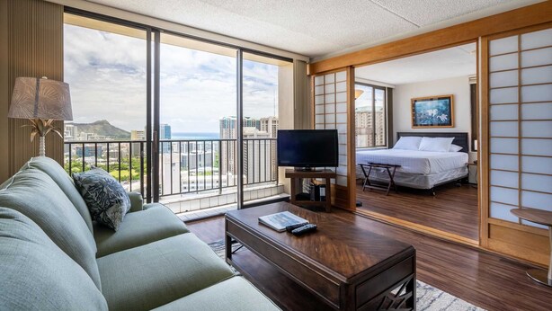 Habitación de hotel con balcón, sofá, televisor, cama y vistas a la ciudad.