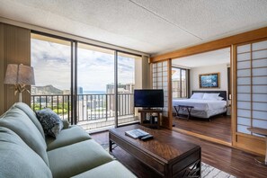 A hotel room with a balcony, a sofa, a TV, a bed, and a view of the city.