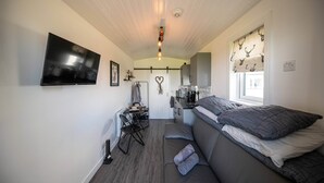 Habitación compacta con cama, televisión, kitchenette y zona de comedor.