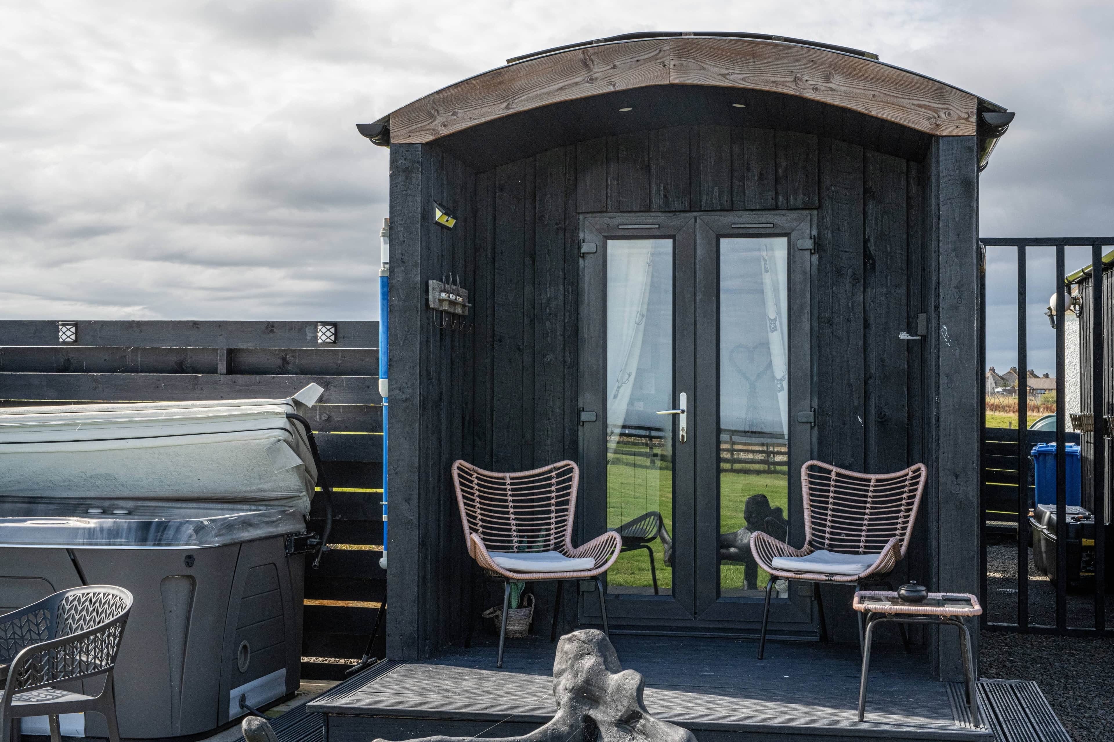 Een klein houten huisje met twee rieten stoelen en een barbecue buiten.