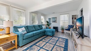 A spacious living room with a teal sectional sofa, a wooden coffee table, a TV on a wooden stand, and a patterned rug.