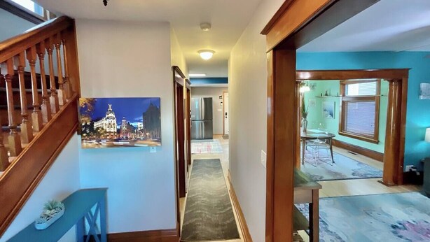 A hallway with a wooden staircase, a stained glass ceiling light, a framed picture on the wall, and a view into a dining area with a table and chairs. - Charming 3 Bdrm by State Fair-Allianz Field -Como (Saint Paul)