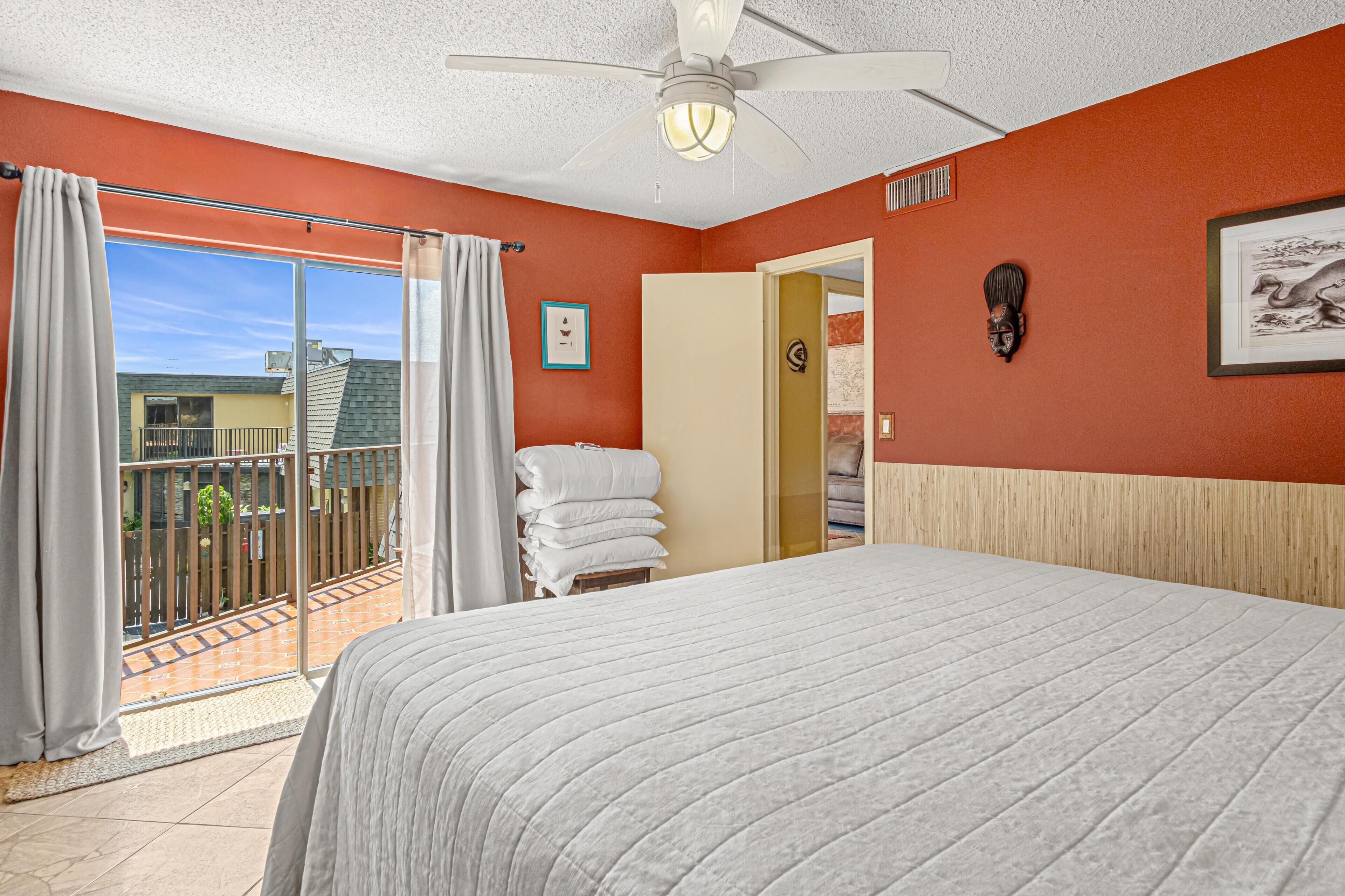 Une chambre d’hôtel avec un grand lit, un ventilateur de plafond, une vue sur le balcon extérieur et une porte donnant sur une autre chambre.