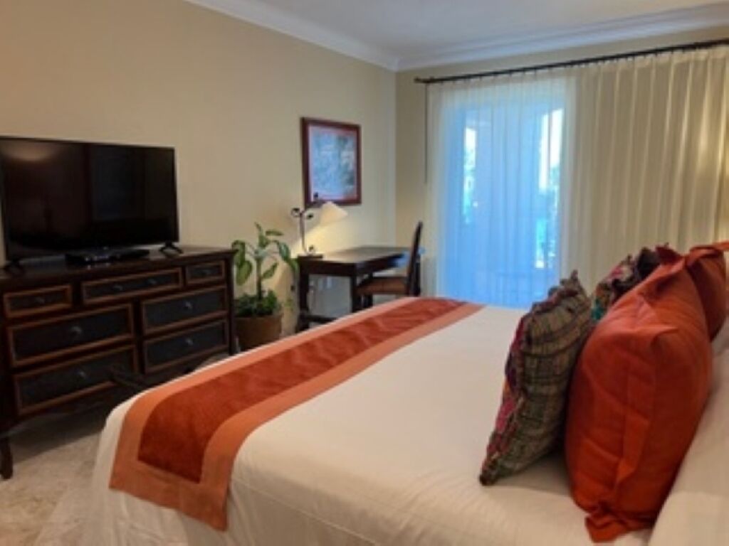 Habitació d'hotel amb llit, televisió, escriptori i finestra amb cortines.