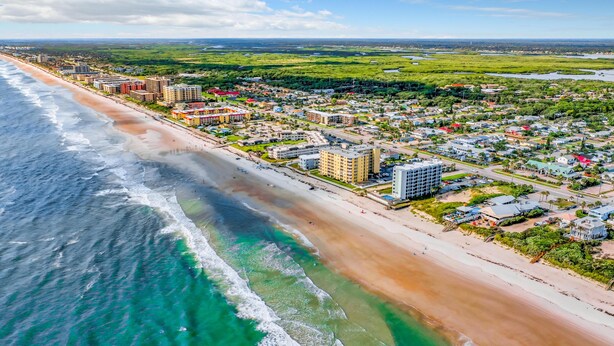 An aerial view of a coastal town with a beach, residential buildings, and a mix of commercial areas.