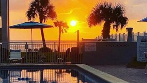 A swimming pool with a sunset view, palm trees, and a fence.